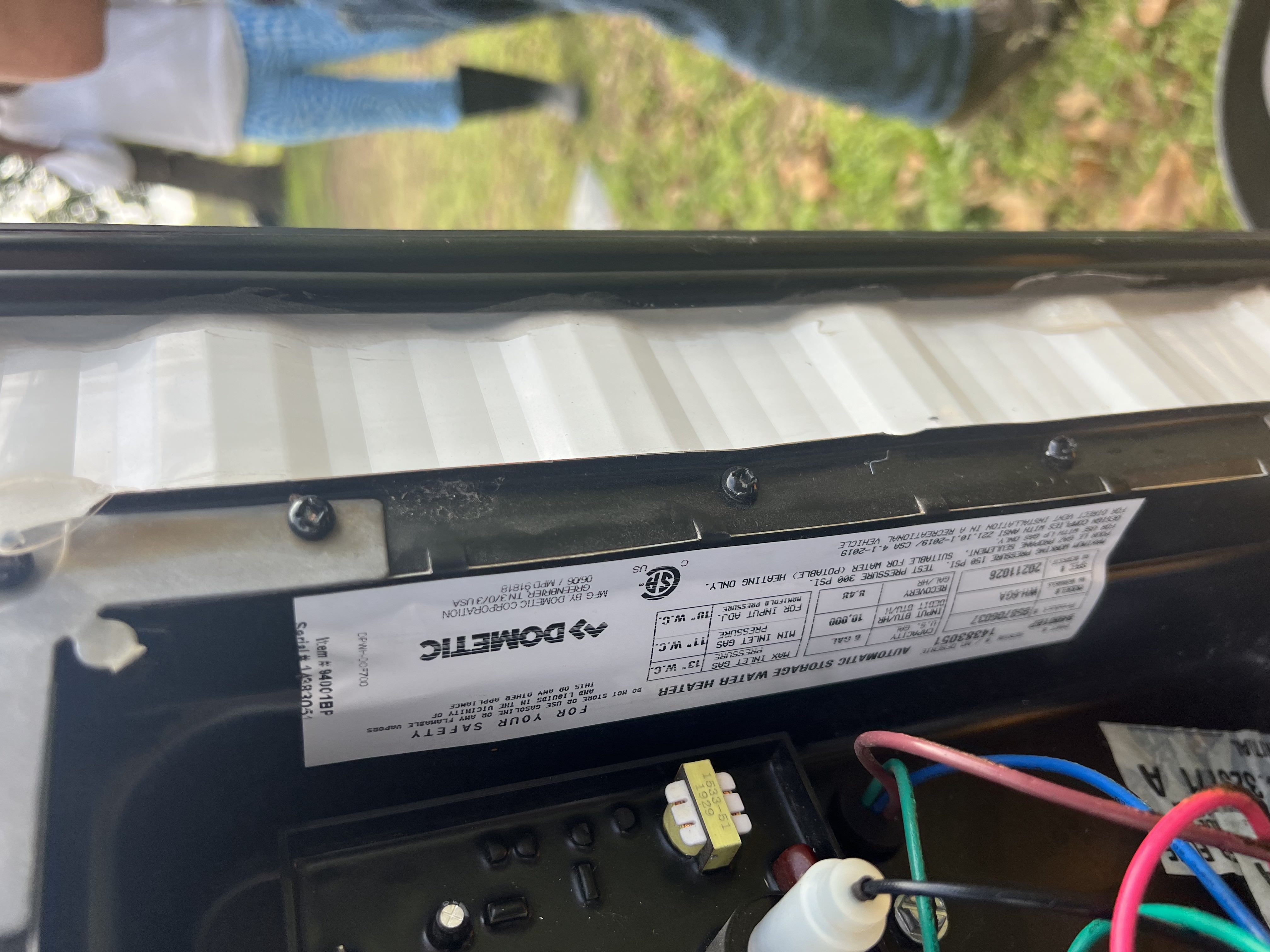 Dometic automatic storage water heater data plate showing model WHN-6A, 6-gallon, 10000 BTU, dated 4-1-2019, with wiring and circuit board visible on the open access door — Boss Bull Mobile RV Services