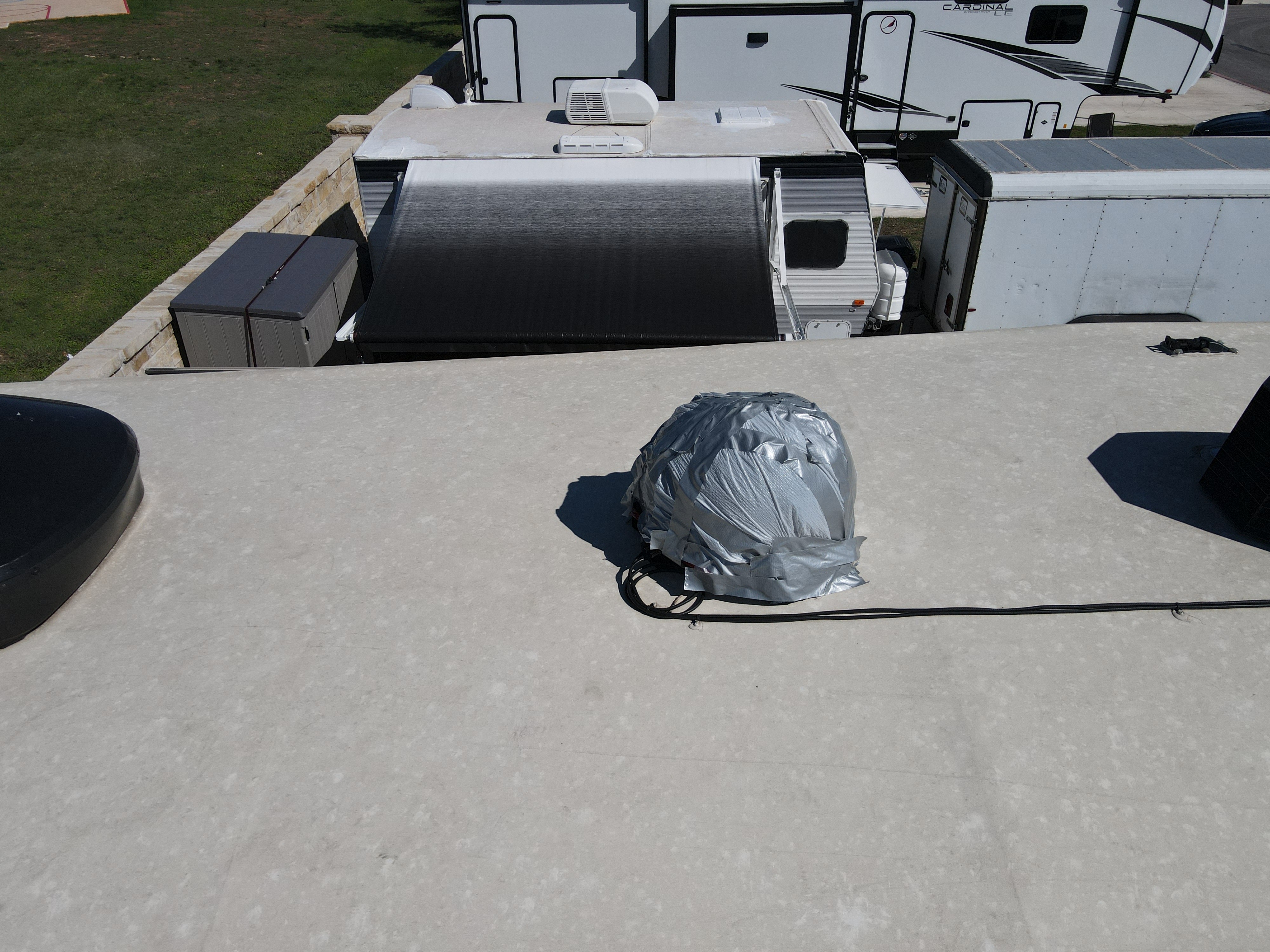 Elevated view of an RV roof with a satellite dome completely wrapped in silver duct tape to cover hail damage — chalky aged membrane background, coaxial cable running across the surface — Boss Bull Mobile RV Services