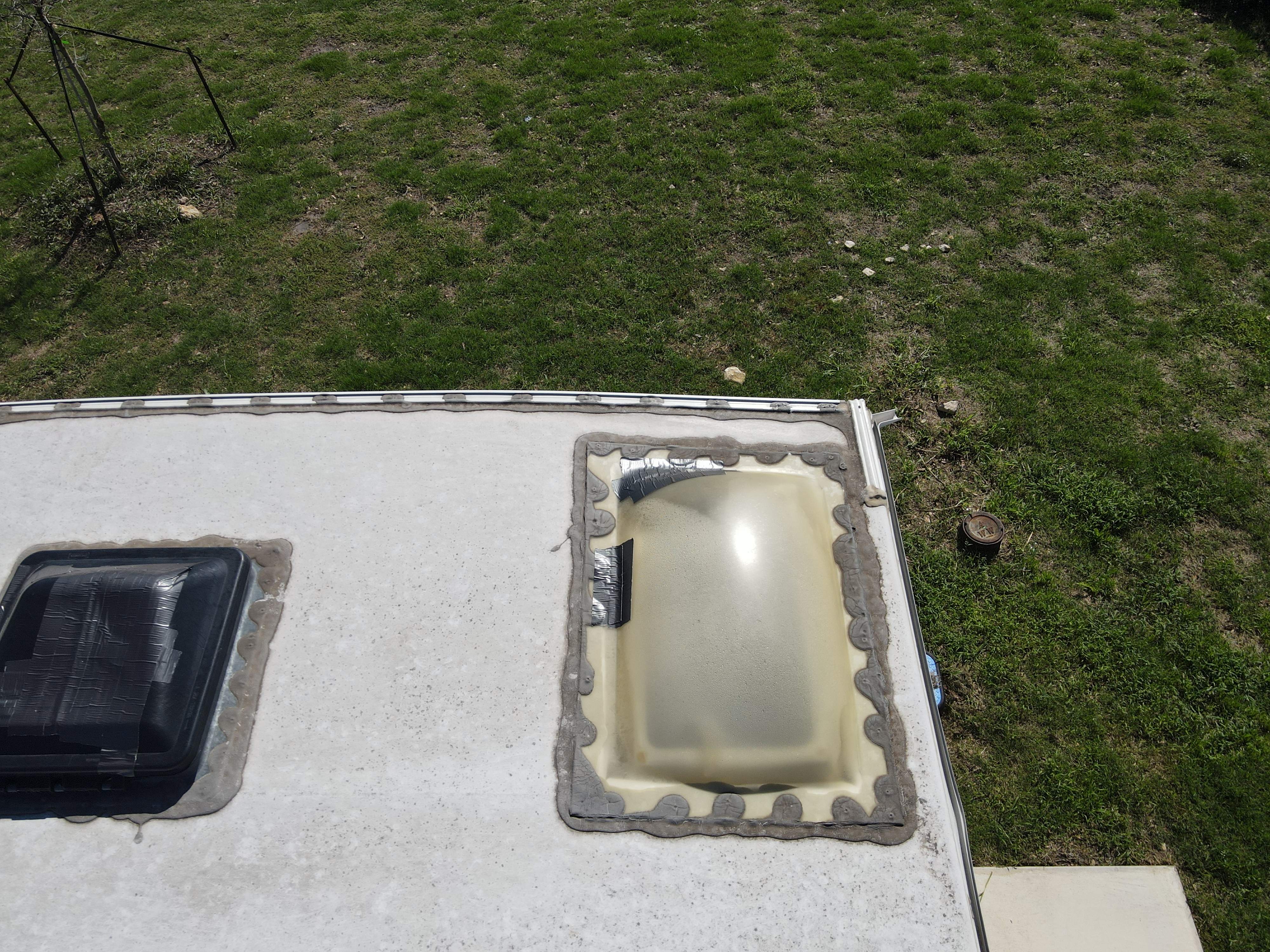 Close overhead view of an RV roof corner showing a duct-tape-patched vent cover and a UV-crazed yellowed skylight dome with blob sealant and a silver duct tape patch — hail damage and failed DIY repair documentation — Boss Bull Mobile RV Services