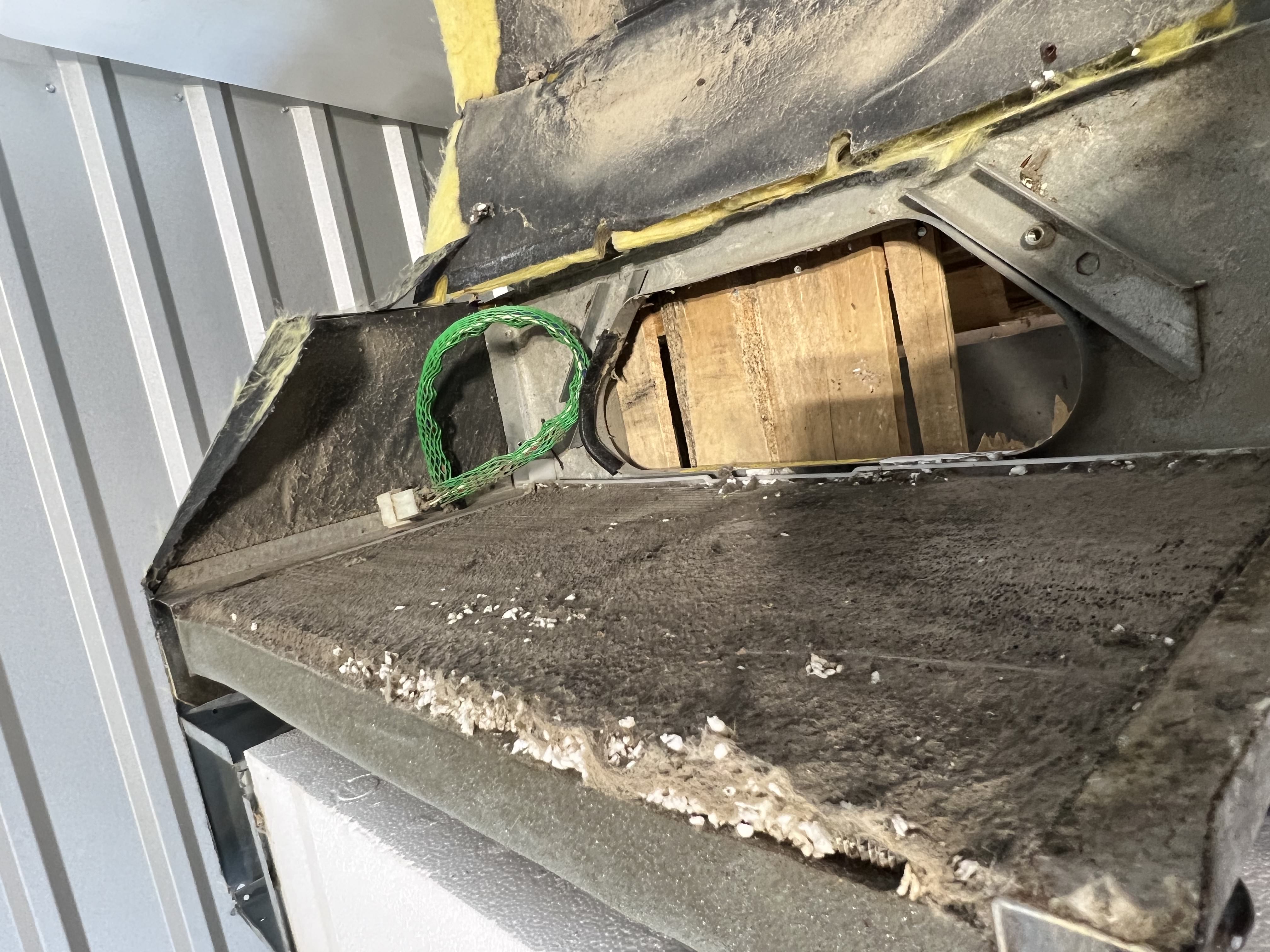 Close-up of an RV rooftop air conditioner condenser fin face packed with debris, dust, and insulation material — the coil surface is uniformly fouled with no clean fin rows visible — Boss Bull Mobile RV Services