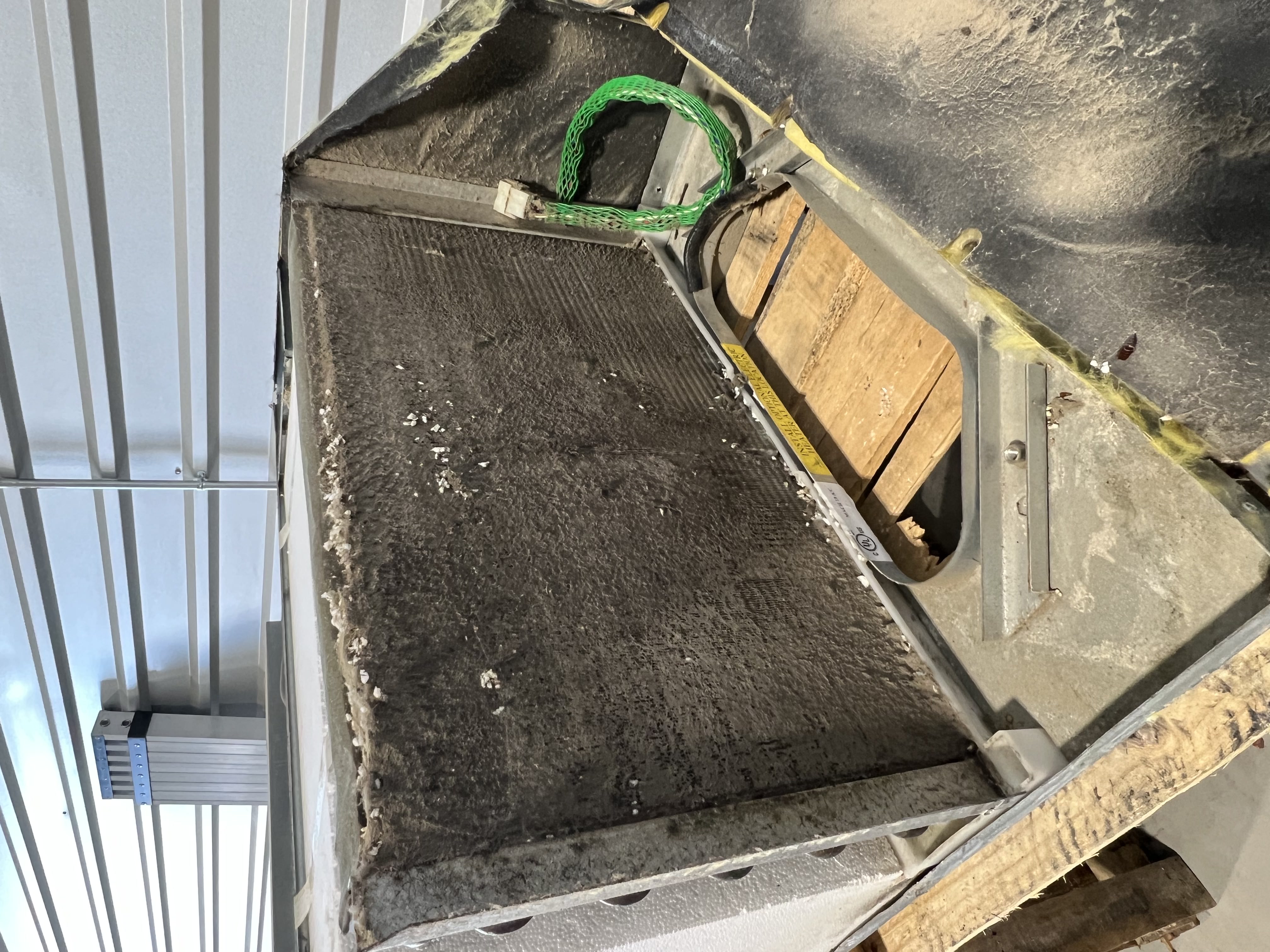 Removed RV rooftop air conditioner unit on a shop floor with shroud off showing the full condenser coil face fouled with debris — Boss Bull Mobile RV Services