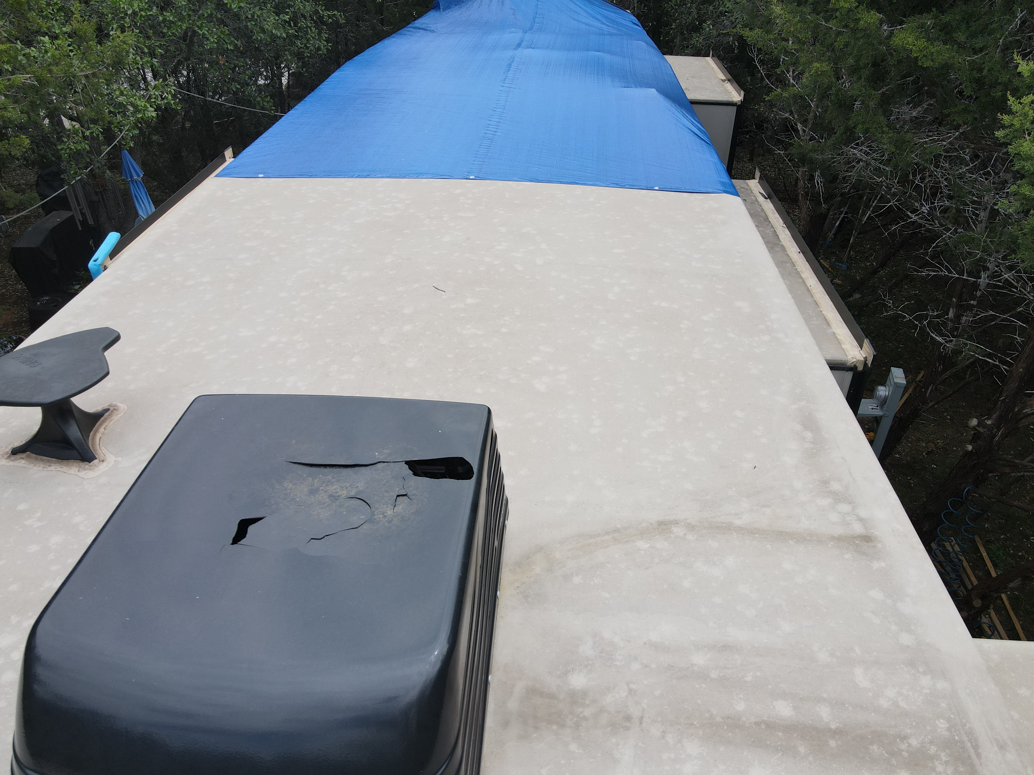 RV AC shroud cracked and breached with temporary blue roof tarp — emergency response for a New Braunfels campground guest during a summer Guadalupe River stay