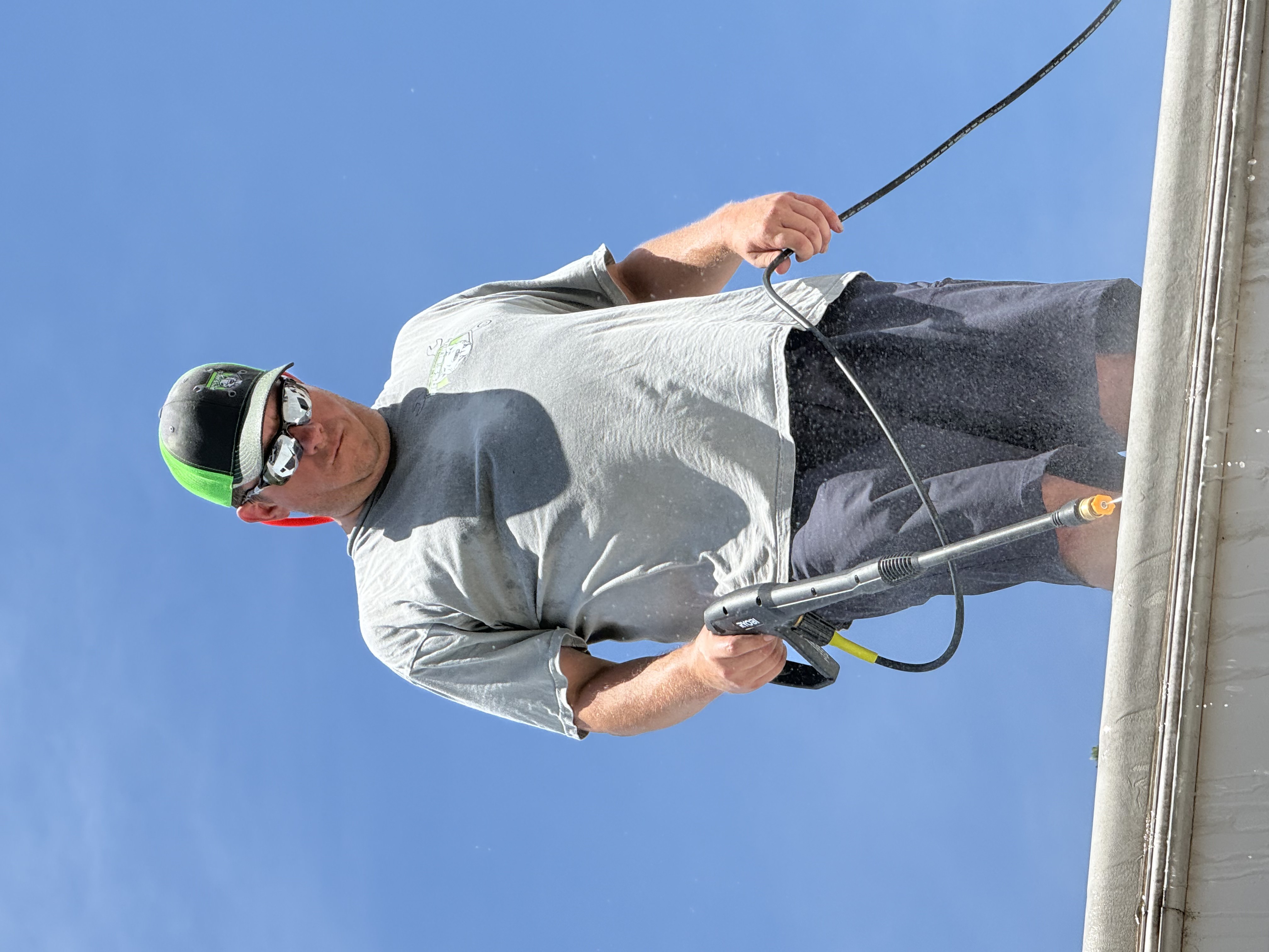 Boss Bull technician standing on an RV roof edge pressure washing the membrane surface during roof cleaning and preparation before coating — blue sky background — Boss Bull Mobile RV Services