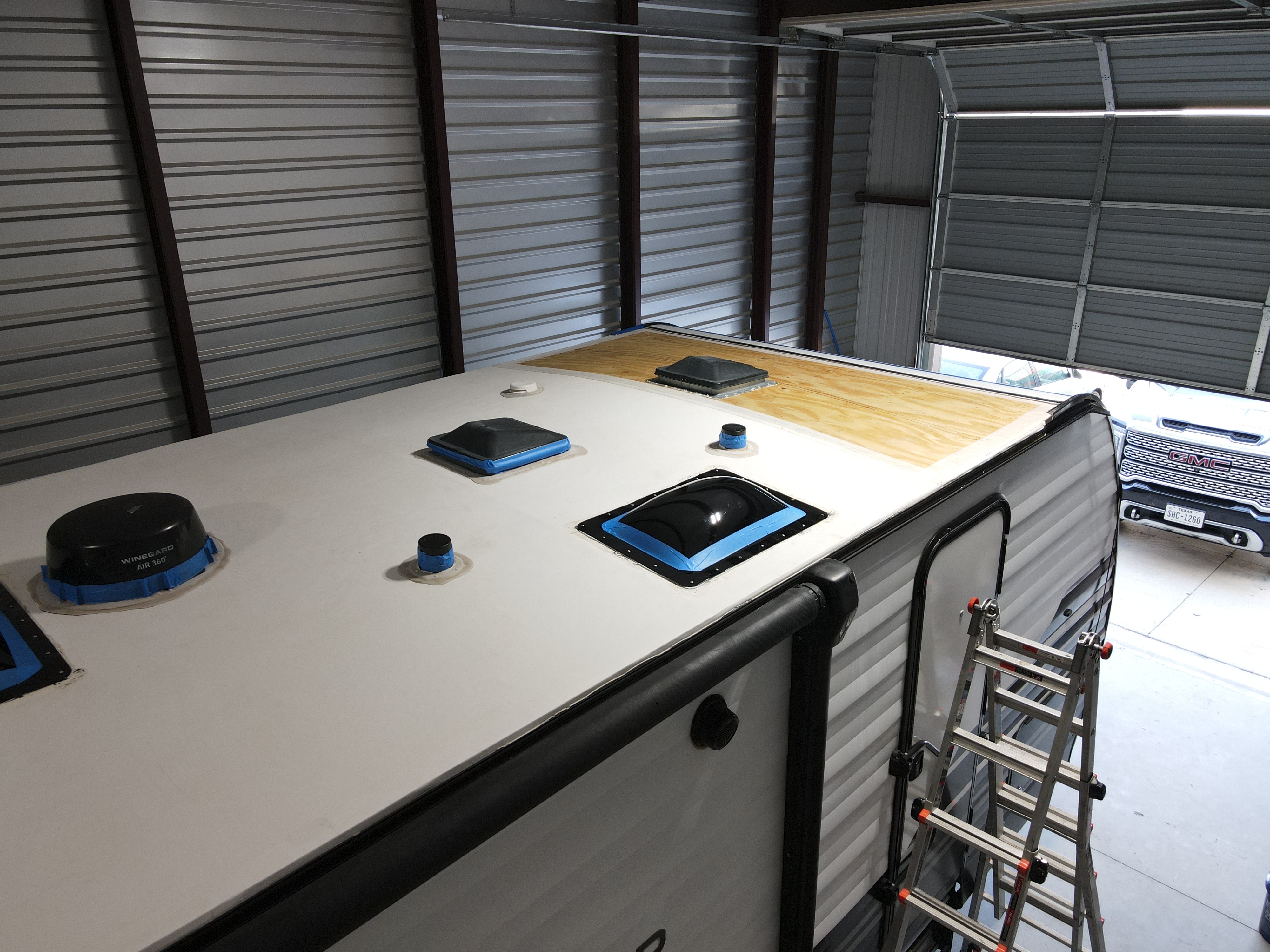 RV in a shop bay during a full roof replacement — new plywood decking exposed in the rear third of the roof while new white membrane is partially installed over the front two-thirds — penetrations in mid-reinstallation — Boss Bull Mobile RV Services