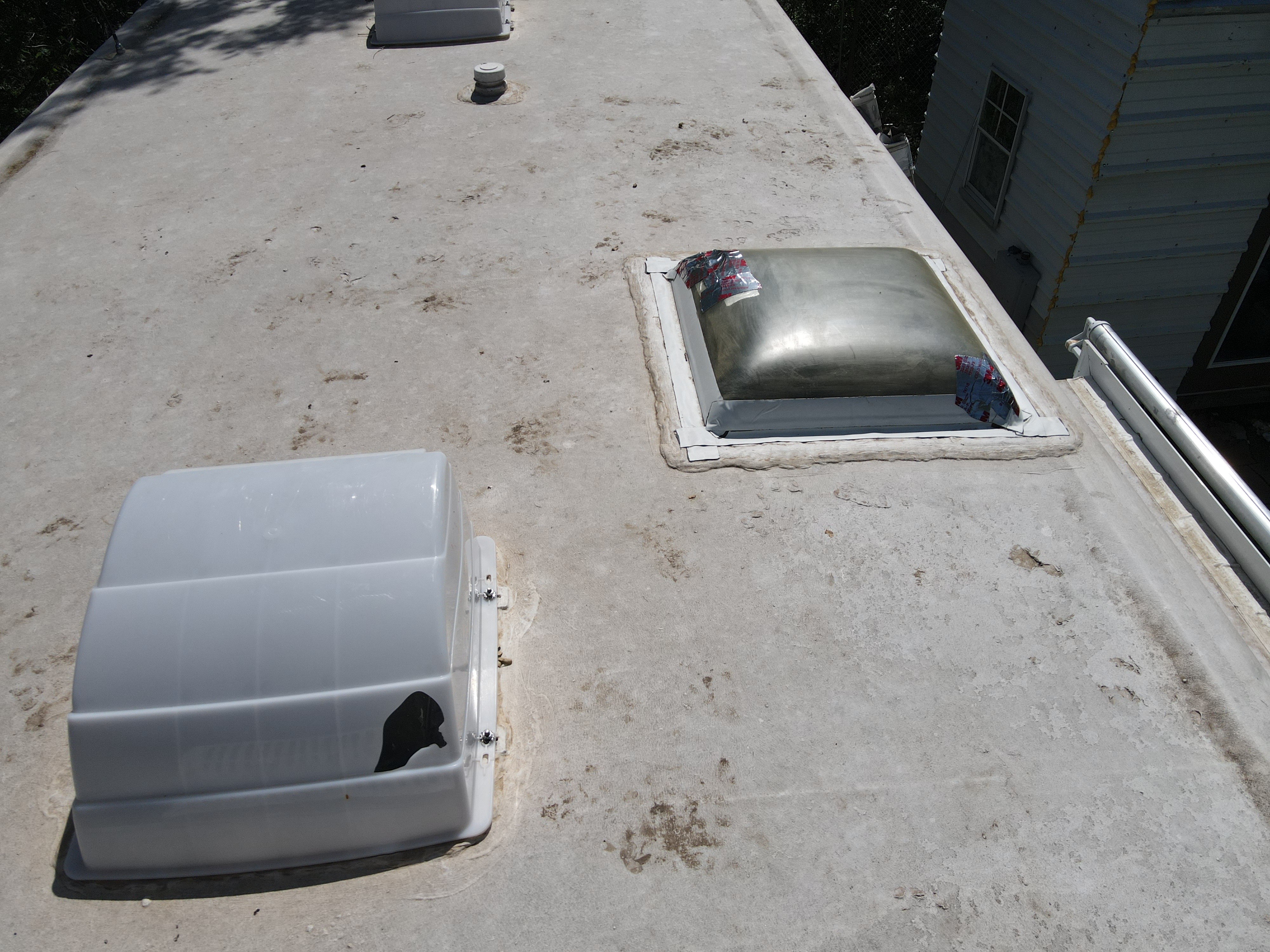 Elevated view of a gray oxidized RV rubber roof with a cracked dome vent base and failing lap sealant around a skylight penetration — pre-repair condition documented during a leak detection service visit — Boss Bull Mobile RV Services