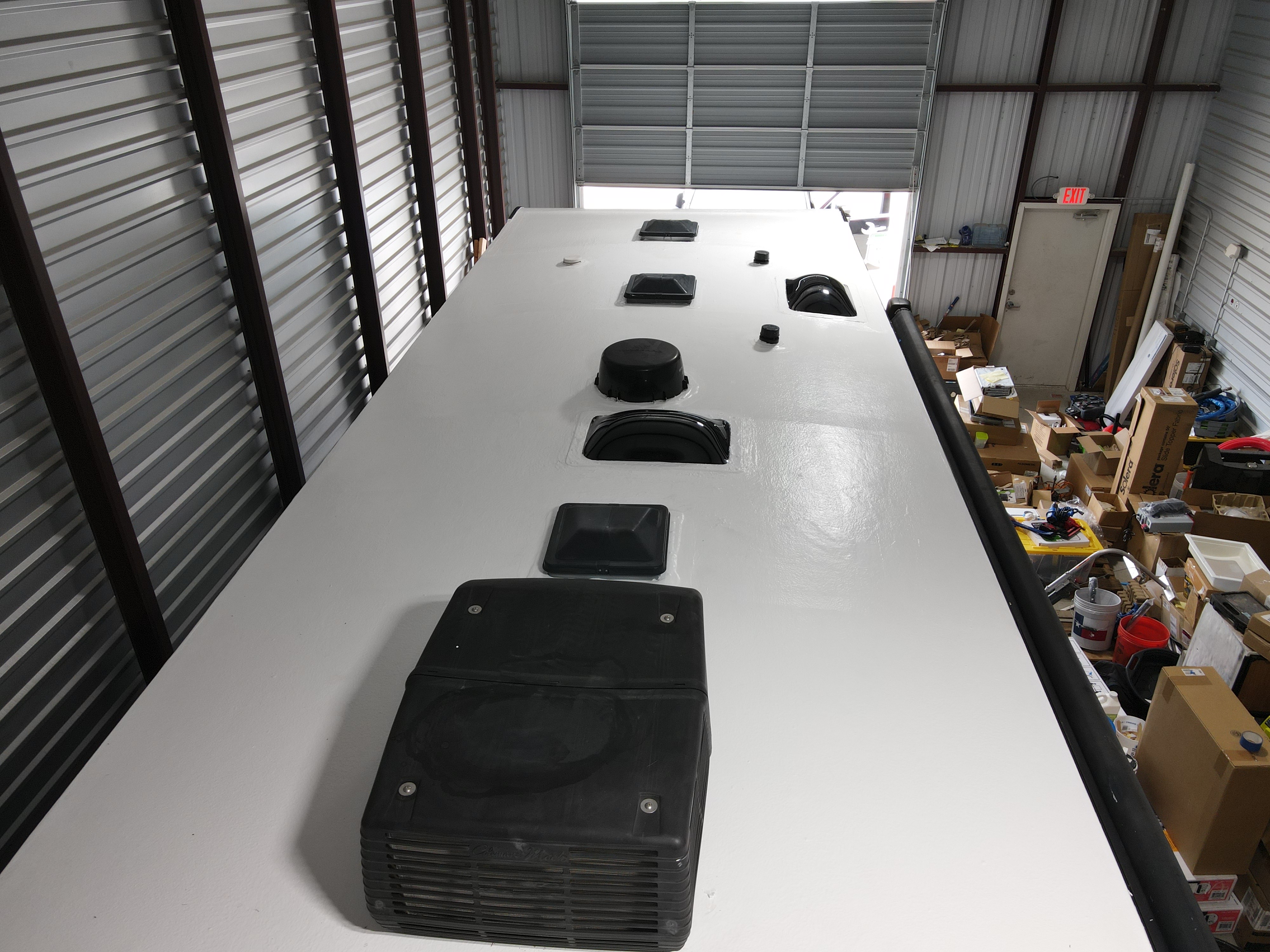 Shop interior overhead view of a completed RV roof restoration on a Crossroads Cameo fifth-wheel — bright white elastomeric coat fully applied, all six penetrations reinstalled and sealed — Boss Bull Mobile RV Services