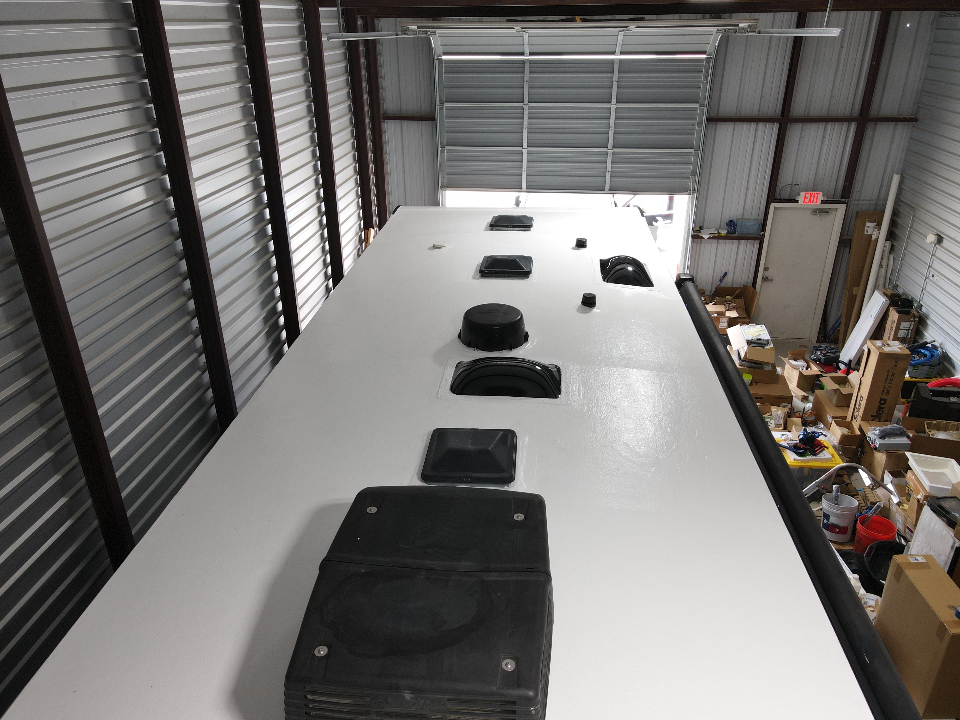 Shop interior overhead view of a completed RV roof restoration on a Crossroads Cameo fifth-wheel — white elastomeric coat fully applied, all penetrations reinstalled and sealed — Boss Bull Mobile RV Services