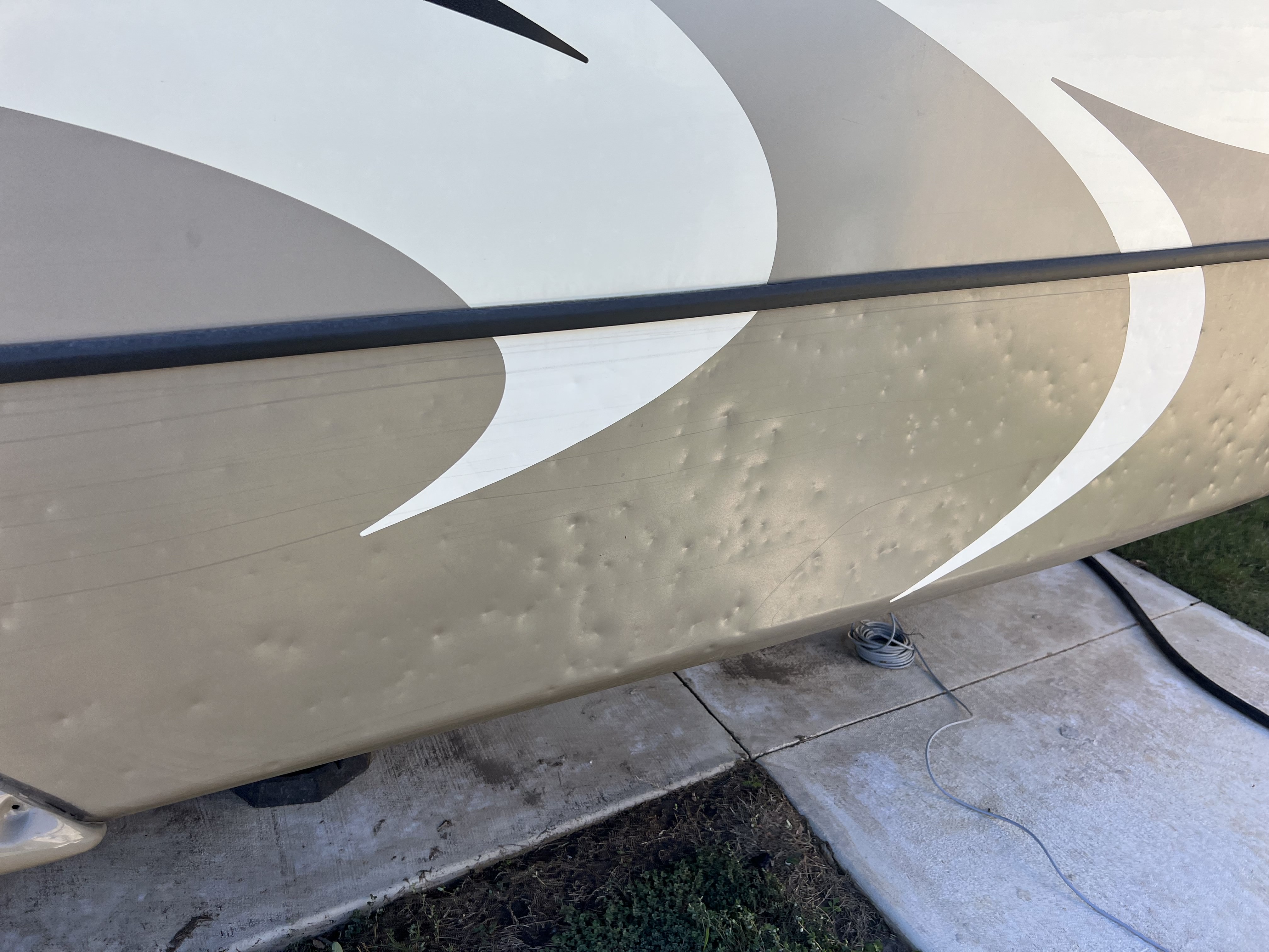 RV exterior sidewall panel showing dozens of circular hail impact dimples below the J-rail molding — hail damage documentation — Boss Bull Mobile RV Services
