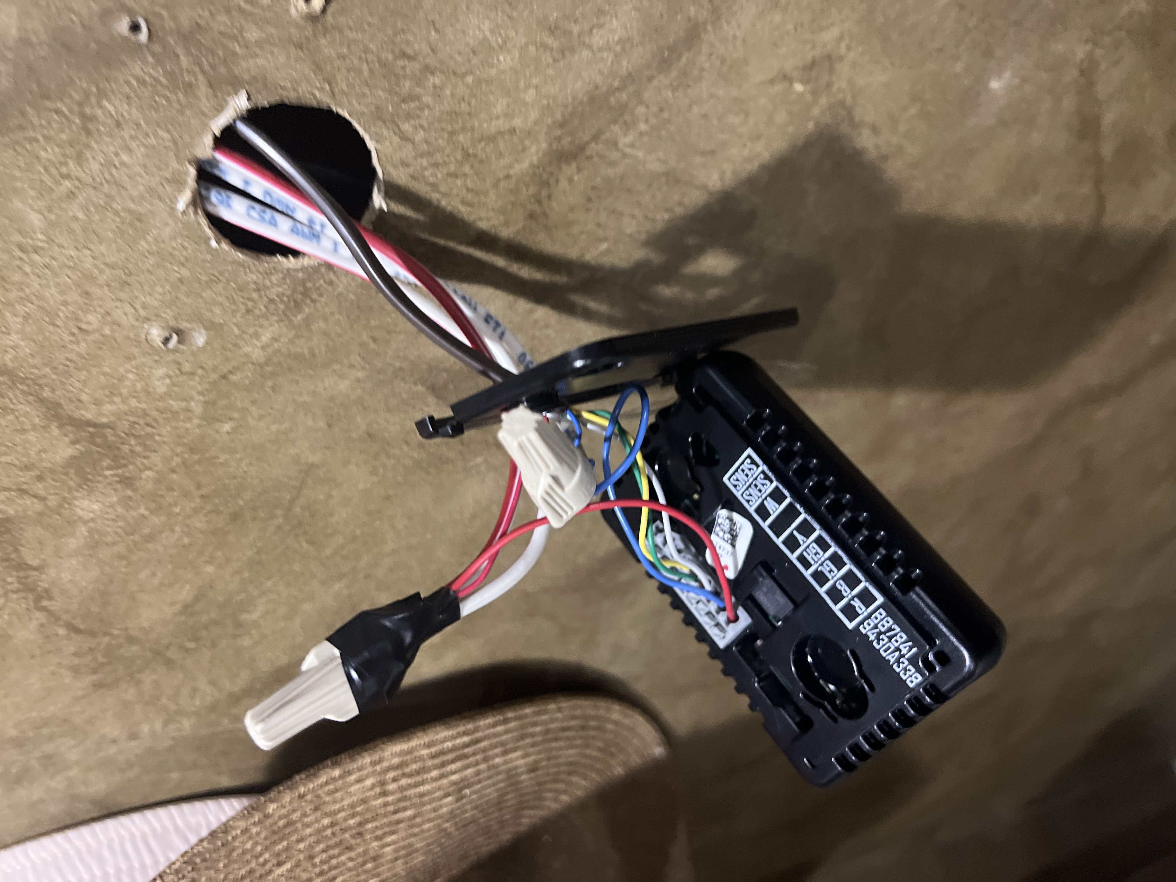 RV wall thermostat control module pulled from the wall mount exposing multi-color low-voltage wiring harness — HVAC control replacement documented during a furnace and thermostat service call — Boss Bull Mobile RV Services