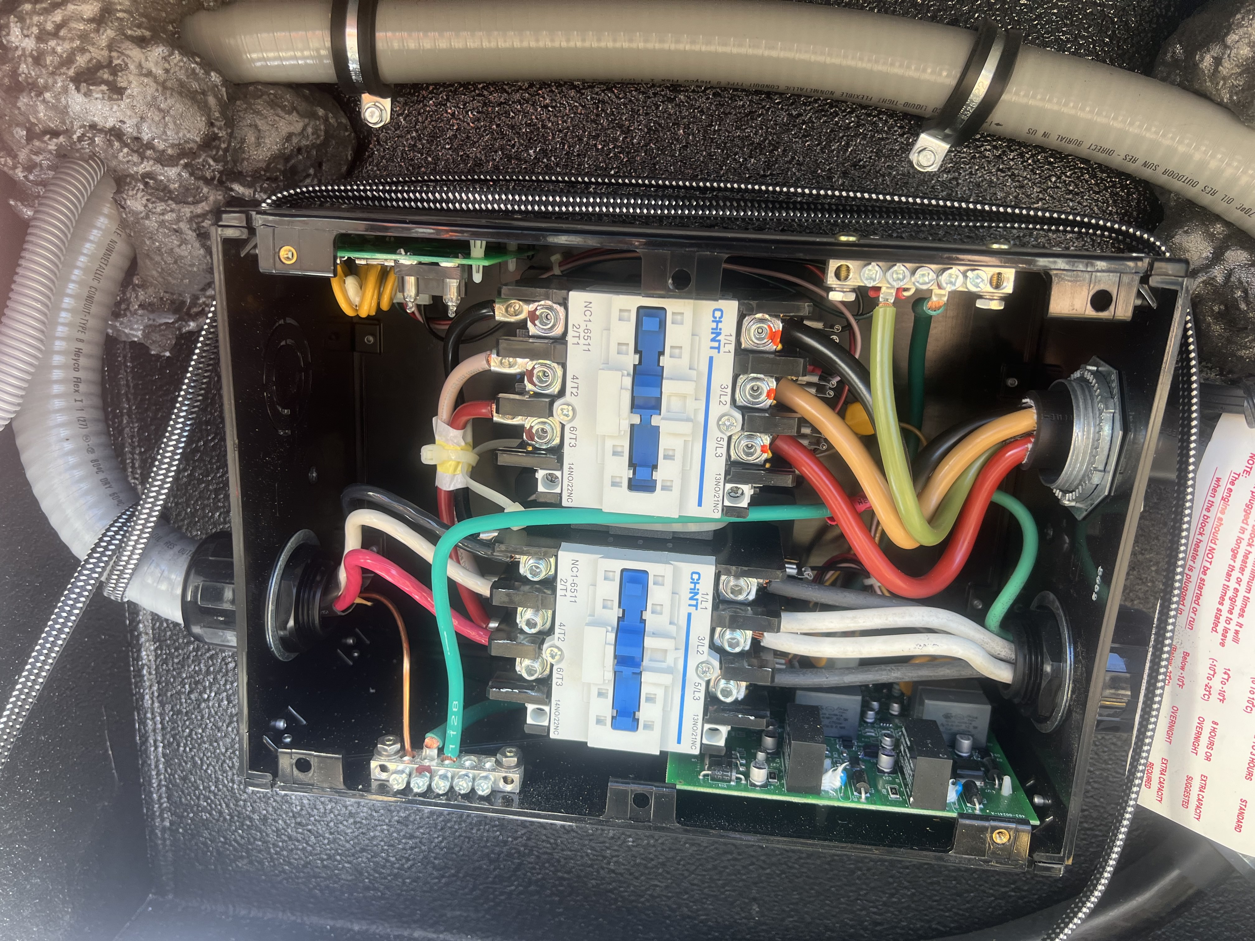 Open RV electrical enclosure photographed in its installed position inside the RV compartment showing two CHNT NC1-6511 contactors, multi-color conductors, control board, and surrounding foam insulation and wiring conduit — Boss Bull Mobile RV Services